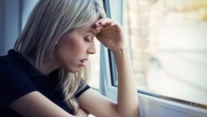 Femme pensive près d’une fenêtre, main au front — remise en question de ses choix amoureux.
