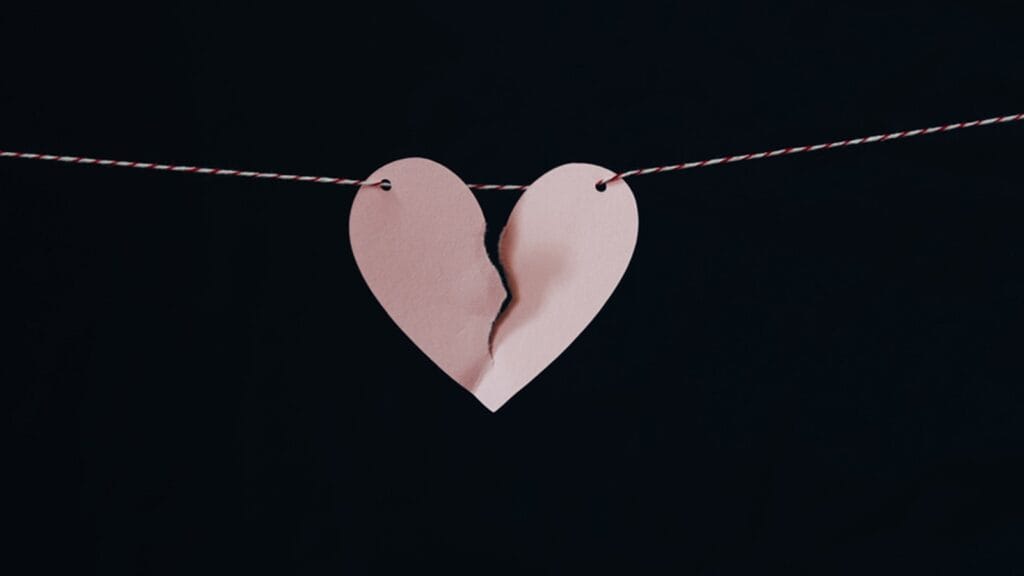 Cœur en papier déchiré suspendu sur fond noir — symbole du ghosting.
